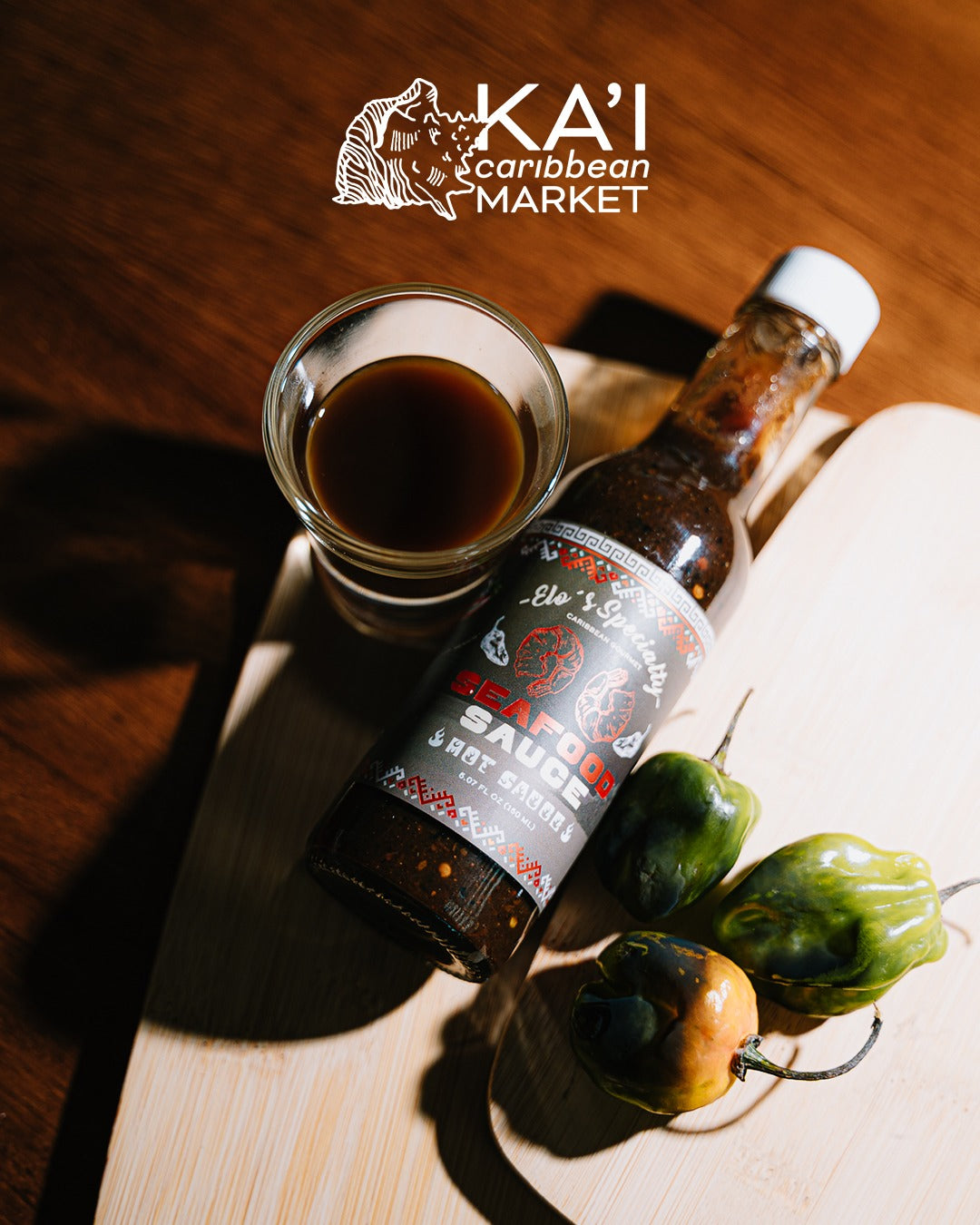 Kai Caribbean Market Seafood Sauce bottle with habanero peppers and a cup of sauce on a wooden board